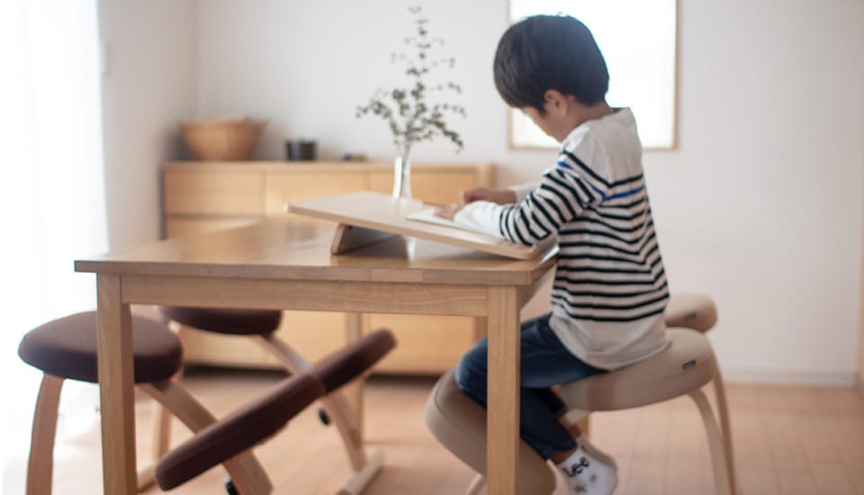 写真:バランスイージーに座った子どもが勉強している様子。4人掛けの机にバランスイージーが4脚用意されている。